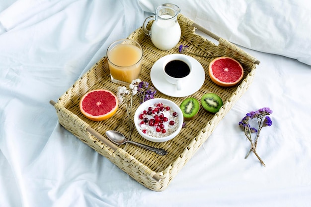 Plateau en osier avec nourriture et boisson sur un lit blanc