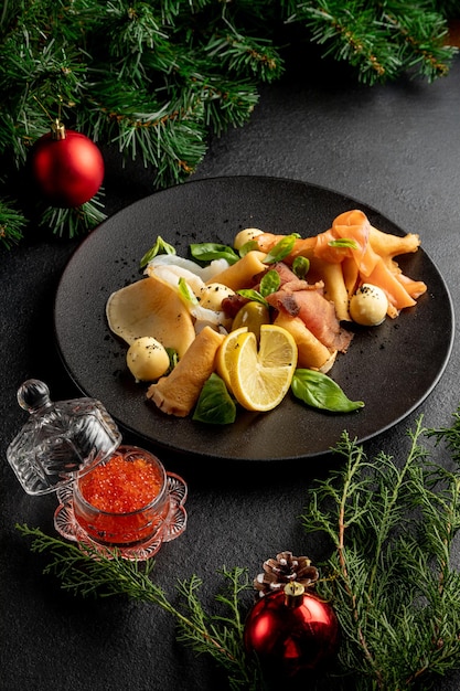 Plateau de poisson sur une plaque noire avec du caviar rouge sur fond sombre de Noël avec des jouets de Noël et des branches d'épinette