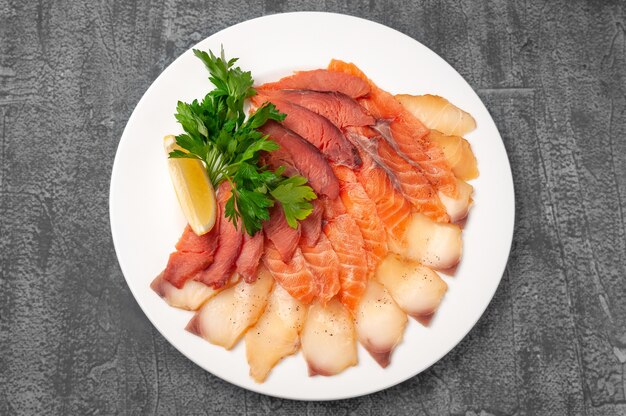 Plateau de poisson saumon et poisson gras. Sur une grande assiette blanche. Garni d'une tranche de citron et d'herbes. Vue d'en-haut. Sur un fond de béton gris.