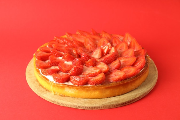 Plateau rond avec tarte aux fraises sur fond rouge.