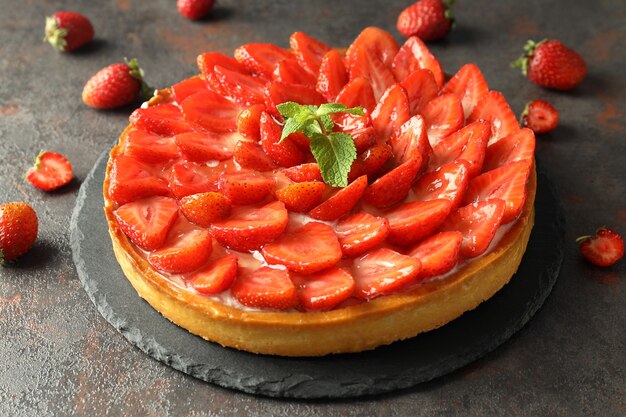 Plateau avec tarte aux fraises sur table texturée sombre.