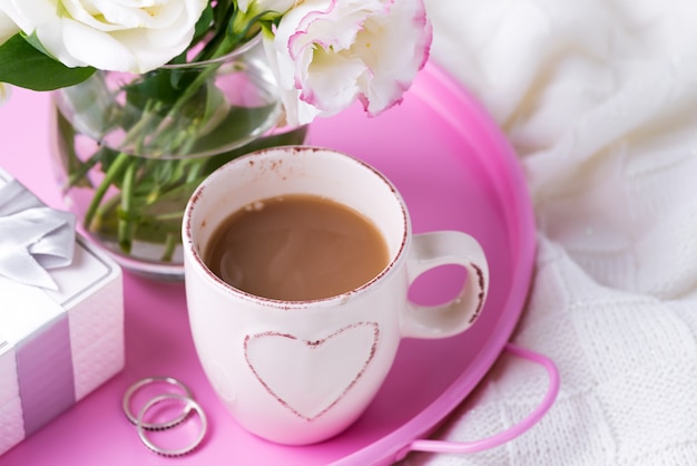 Un plateau avec une tasse de café, une boîte-cadeau, des fleurs et des anneaux sur le lit