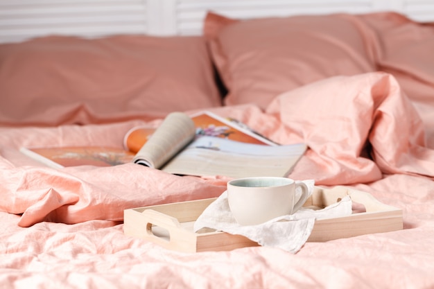 Un plateau avec une tasse de lettre d'amour de thé chaud et des magazines au lit