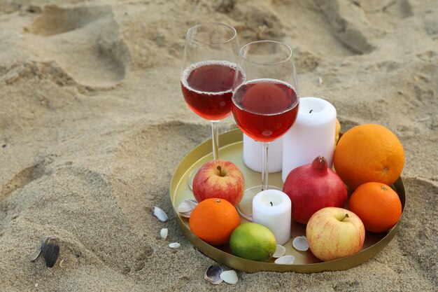 Plateau avec verres de vin, fruits et bougies sur la plage de sable de la mer