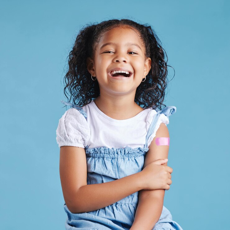 Photo plâtre heureux et portrait d'un enfant en studio pour une injection de vaccin ou de booster médical soins de santé excités et fille du mexique avec un bandage sur le bras pour la vaccination par fond bleu