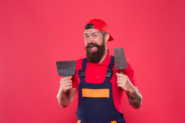 Photo plâtrier hipster constructeur en casquette fond rouge architecte d'intérieur ouvrier barbu avec des outils de plâtrage plâtrier professionnel plâtrier habile rénovation réussie réussite de la réparation