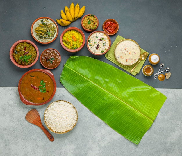 Plats d'accompagnement de fête traditionnels du Kerala disposés dans un fond bicolore avec des feuilles de bananier fraîches