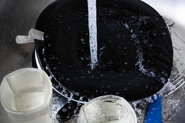Plats et verres noirs sous l'eau dans l'évier