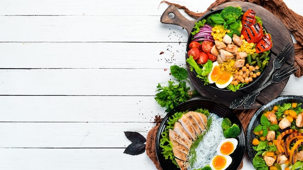 Plats de viande de poulet et de légumes dans une assiette noire sur un fond en bois blanc Coupe de Bouddha Vue de dessus Espace libre pour votre texte