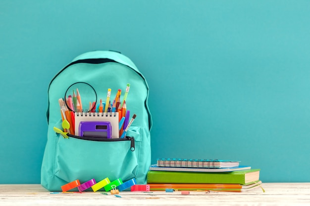 Plein bleu école sac à dos avec des fournitures différentes sur fond bleu.