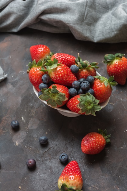 Plein de bol en céramique avec des myrtilles et des fraises sur la table en pierre.