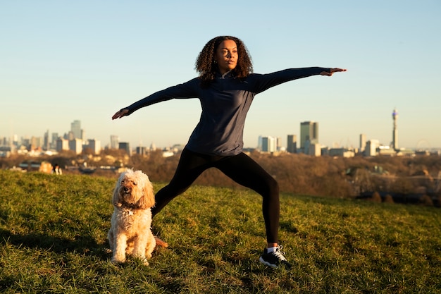 Photo plein coup femme faisant du yoga avec un chien à l'extérieur