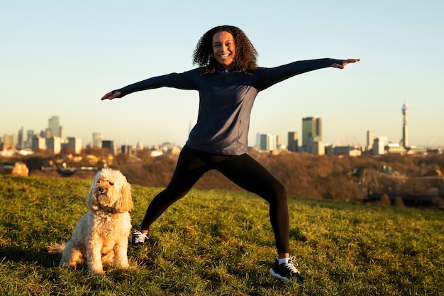 Photo plein coup femme faisant du yoga avec un chien à l'extérieur