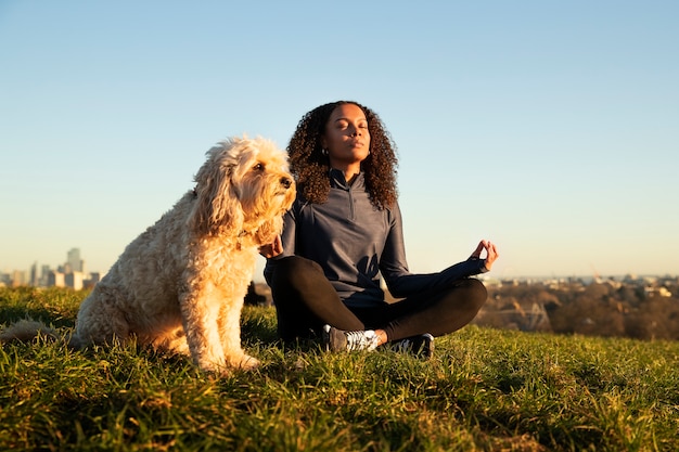 Photo plein coup femme faisant du yoga avec un chien à l'extérieur