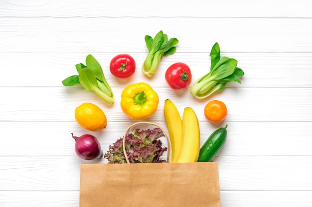 Plein sac en papier écologique de différents aliments de santé - poivron jaune, tomates, bananes, laitue, vert, concombre, oignons Vue de dessus Mise à plat Épicerie