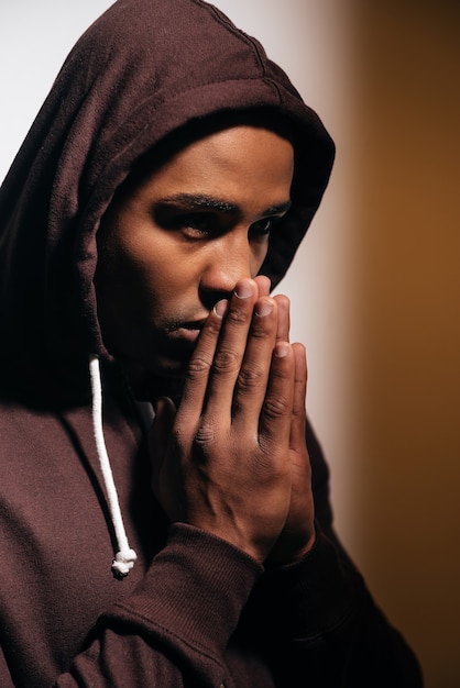 Pleine concentration. Confiant jeune homme africain en chemise à capuchon gardant les mains jointes près du visage