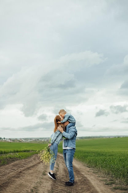 Pleine croissance tourné jeune famille en vêtements décontractés en denim se promenant dans le parc en se tenant la main le jour du printemps chaud