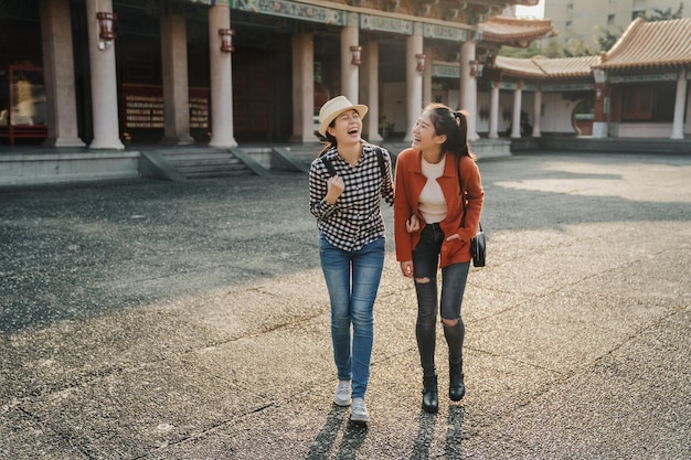 pleine longueur deux jeunes amies asiatiques marchant en visite dans le temple chinois de confucius parler bavarder rire joyeux. les femmes touristiques se détendent aux beaux jours avec la lumière du coucher du soleil joyeuse souriante avec une blague