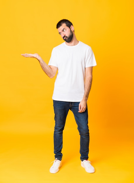 Pleine longueur homme à la barbe sur mur jaune isolé tenant la surface avec des doutes