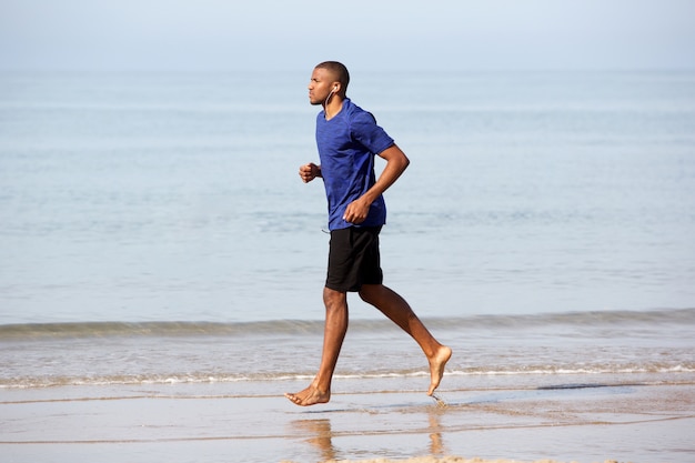 Pleine longueur jeune homme noir jogging le long de la plage