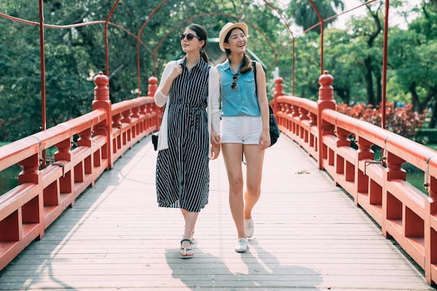 pleine longueur avec vue de face de joyeux visiteurs asiatiques apprécient le design tout en marchant ensemble sur un pont rouge japonais pendant l'été ensoleillé.