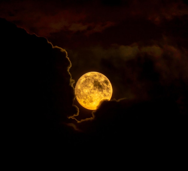 Pleine lune rouge passant ou émergeant des nuages en silhouette éclairée par le clair de lune