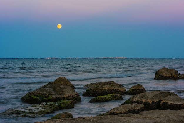 Une pleine lune se lève sur l'eau à la plage.