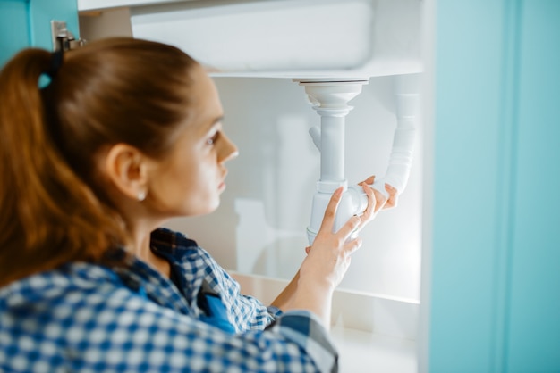 Plombier Féminin En Uniforme Installant Un Tuyau D'évacuation Dans La Cuisine. Bricoleur Avec évier De Réparation De Sac à Outils, Service D'équipement Sanitaire à Domicile