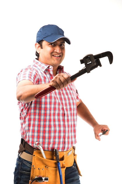 Photo plombier indien tenant un rouleau de dessin et une clé à pipe ou une clé de plomberie ou un smartphone, debout isolé