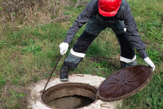 Un plombier masculin a ouvert le trou d'homme d'un puits d'eau pour l'inspection et la réparation préventives