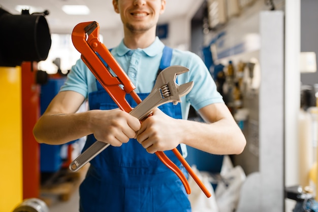 Le plombier pose avec des clés à pipe à la vitrine du magasin de plomberie. Homme achetant des outils et des équipements d'ingénierie sanitaire en magasin