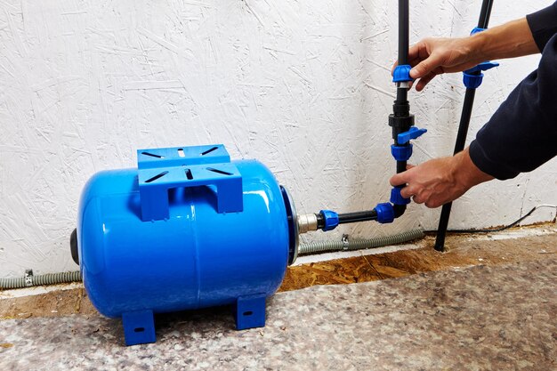 Photo le plombier relie le réservoir à pression de stockage d'eau au système d'approvisionnement en eau domestique à l'aide de tuyaux en hdpe reliés par un raccord de compression