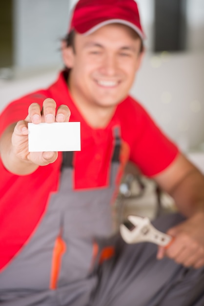 Plombier tenant une clé dans la main et montrant la carte de visite.