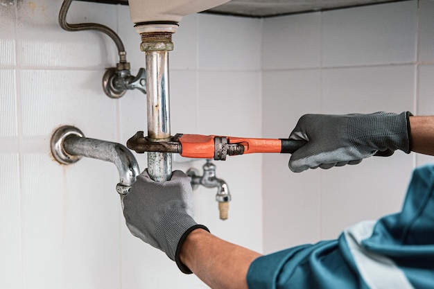 Photo plombier utilisant une clé pour réparer le tuyau d'eau sous l'évier.