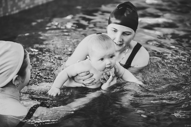 Plongée Bébé Dans La Pataugeoire. Jeune Maman, Instructeur De Natation, Heureuse Petite Fille. Apprenez à Nager. Profitez De La Première Journée De Baignade Dans L'eau. Mère Tenant Bébé Et Plongée. Noir Et Blanc