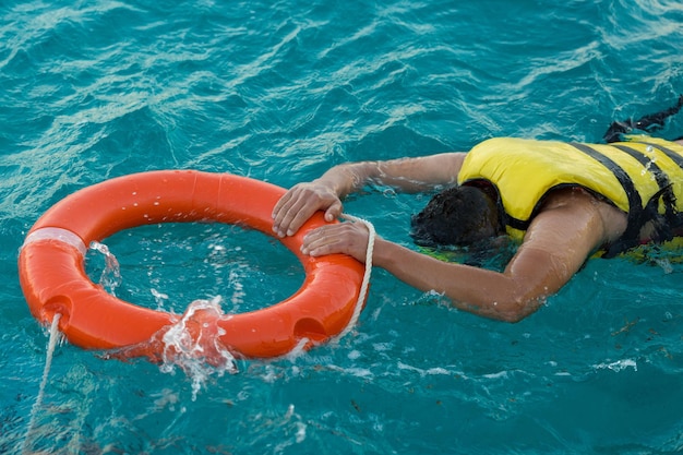 Un plongeur barbu dans un gilet de sauvetage s'accroche à une bouée de sauvetage dans l'eau de mer azur transparente