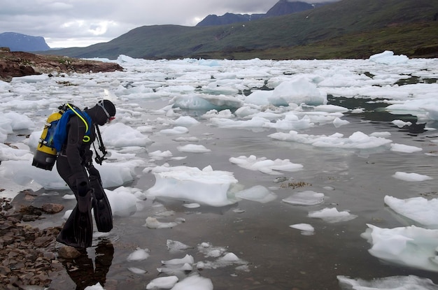 Plongeur entrant dans un lac de montagne couvert de petits icebergs