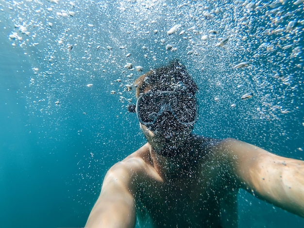 Le plongeur masculin nage dans la mer sous l'eau avec un masque et un tuba prend un selfie de votre visage