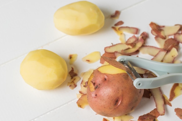 Éplucheur et pommes de terre sur une table en bois blanche. Équipement spécial pour le nettoyage des légumes .