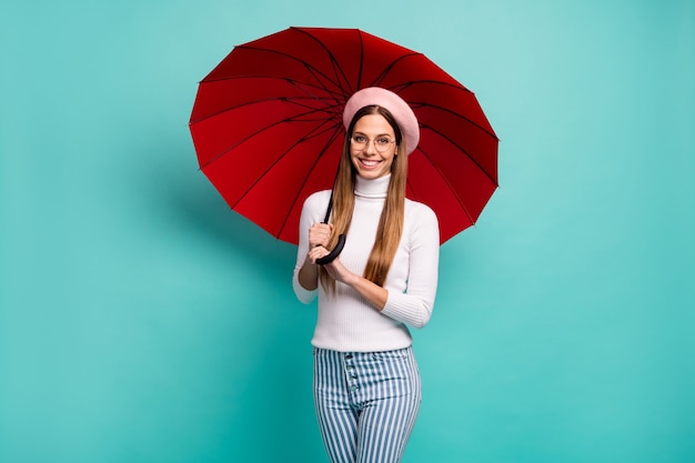 La pluie ne m'arrêtera pas. Photo d'une jolie dame de voyage tenant un grand parapluie rouge à pied dans la rue à l'étranger bonne humeur porter des spécifications béret rose col roulé blanc jeans rayés fond de couleur sarcelle isolé