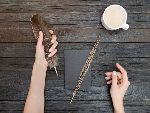 Plume dans une main féminine, un cahier et une tasse de café. Ancienne table en bois. Vue de dessus