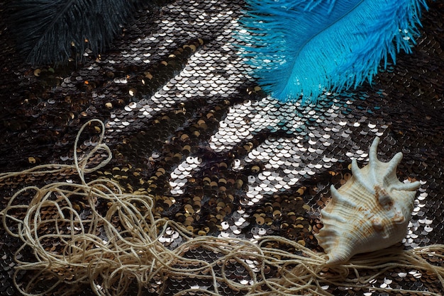 Plumes d'autruche pelucheuses blanches et bleues et une coquille de palourde sur un oreiller avec des paillettes d'or