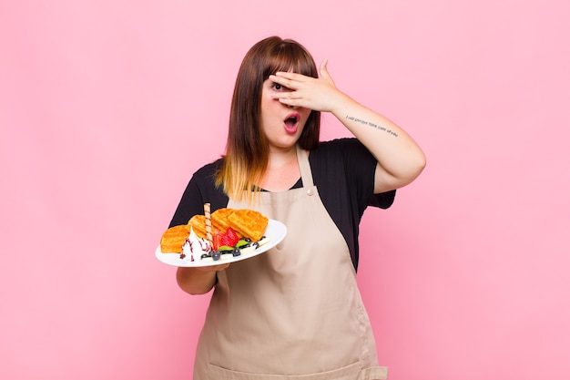 Plus femme de taille à la recherche de choc, effrayé ou terrifié, couvrant le visage avec la main et furtivement entre les doigts