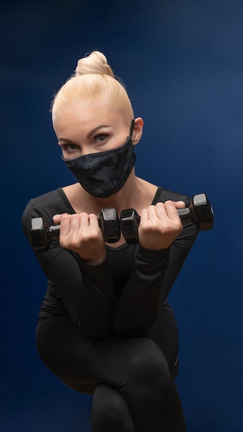 La plus jeune belle dans un masque et avec des haltères regarde la caméra belle ballerine