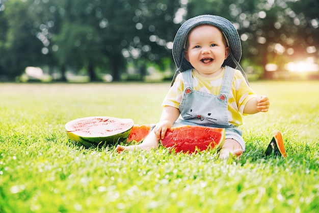 La plus mignonne petite fille souriante mangeant de la pastèque sur l'herbe verte en été Drôle petit enfant heureux mange une collation de fruits sains sur la nature
