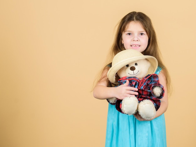 La plus mignonne de tous les temps Kid petite fille étreint soigneusement peluche ours en peluche fond beige Tendres pièces jointes Petite fille tient ours en peluche chapeau de paille En amour avec un ours en peluche mignon Enfance heureuse