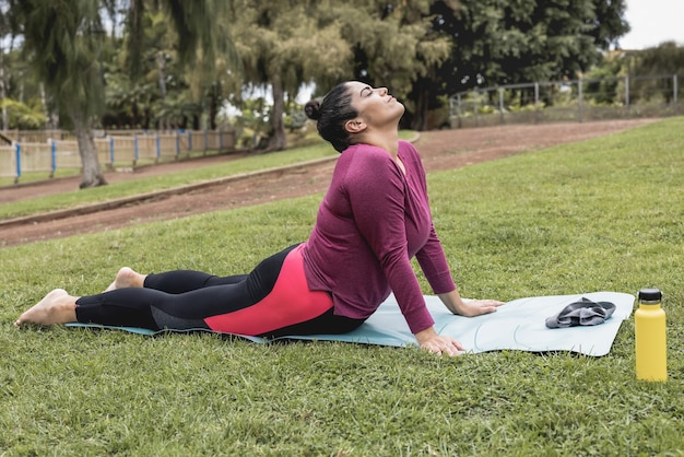 Plus la taille femme faisant une séance de yoga en plein air au parc de la ville - Focus sur le visage