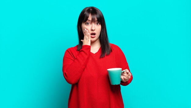 Plus la taille jolie femme se sentant choquée et effrayée, l'air terrifiée avec la bouche ouverte et les mains sur les joues