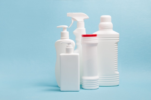 Plusieurs bouteilles en plastique blanc sans étiquettes avec des produits de nettoyage sur une surface bleue