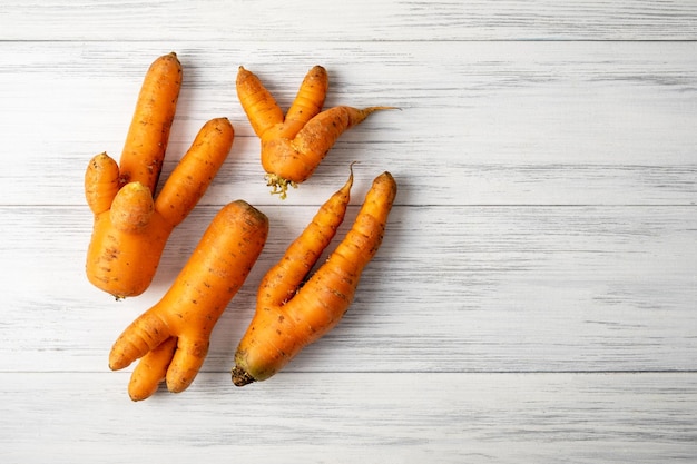 Plusieurs carottes laides orange mûres se trouvent sur une surface en bois clair